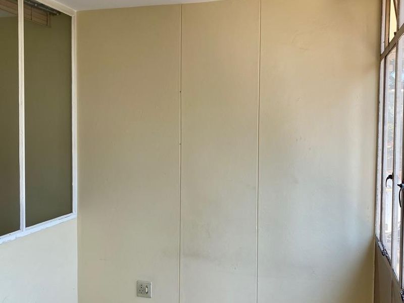 An enclosed balcony or sunroom featuring tiled flooring, aluminum window frames, and neutral wall paneling, offering a versatile space for potential renovation.