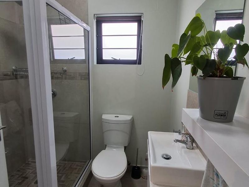 A compact, functional bathroom featuring a glass-enclosed shower, a modern vanity basin, and a toilet, finished with neutral wall and floor tiles.