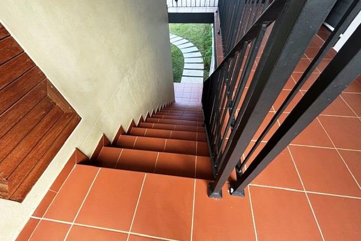 An outdoor staircase featuring terracotta-style tiled steps and a black metal railing, leading down to a paved garden path.