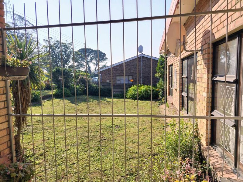 A view of the rear garden and brick exterior wall, featuring security bars on the windows and a satellite dish mounted to the building.
