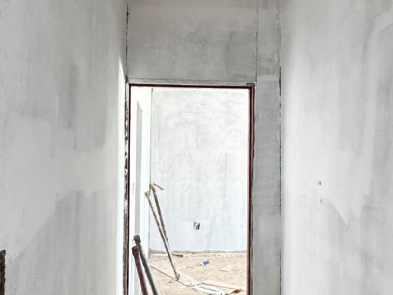 A narrow hallway in a state of construction, featuring unfinished plaster walls and an exposed dirt floor, awaiting final flooring and wall finishes.