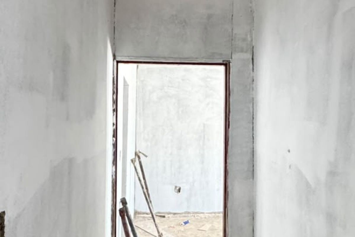 A narrow hallway in a state of construction, featuring unfinished plaster walls and an exposed dirt floor, awaiting final flooring and wall finishes.