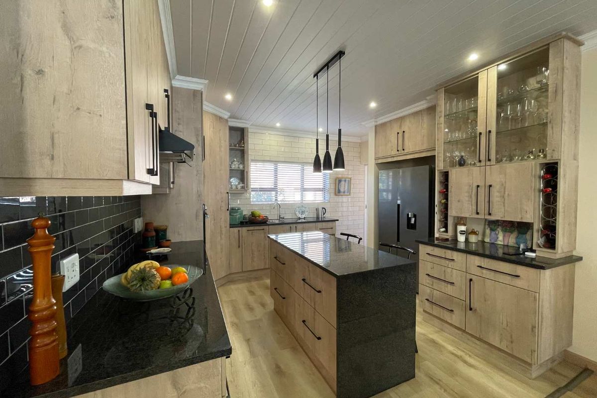 Modern kitchen featuring light wood cabinetry, contrasting black granite countertops, a central island, subway tile backsplash, and stylish pendant lighting.