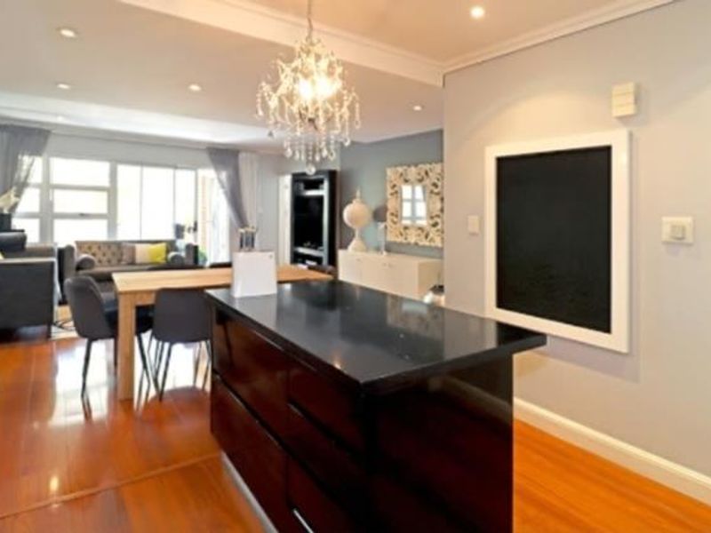 Open plan living area featuring a kitchen island with dark cabinetry, hardwood flooring, and recessed lighting, creating a seamless flow between kitchen and lounge.