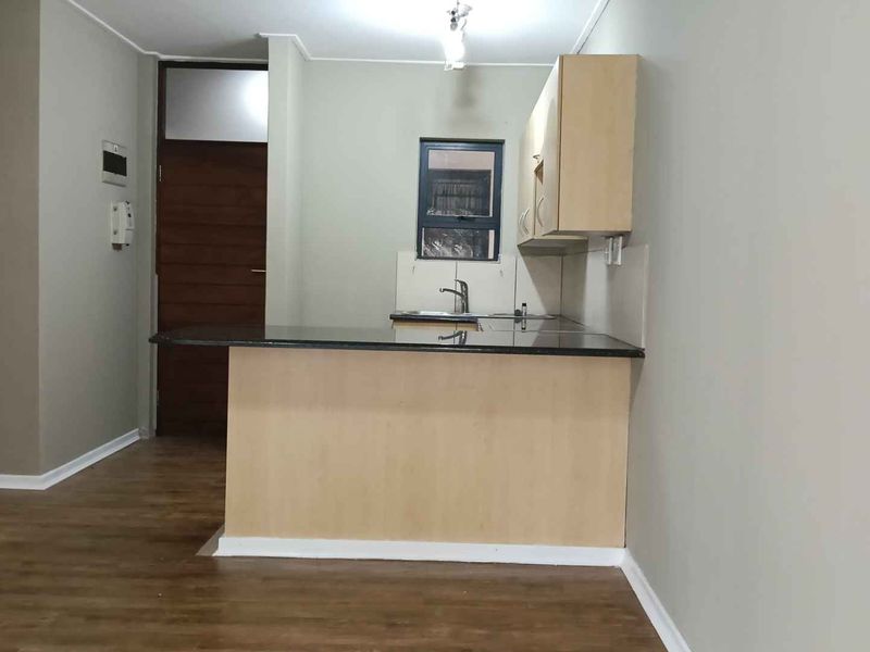 A compact kitchen featuring light wood-tone cabinetry, dark granite countertops, and a stainless steel sink, set against neutral walls with laminate flooring.