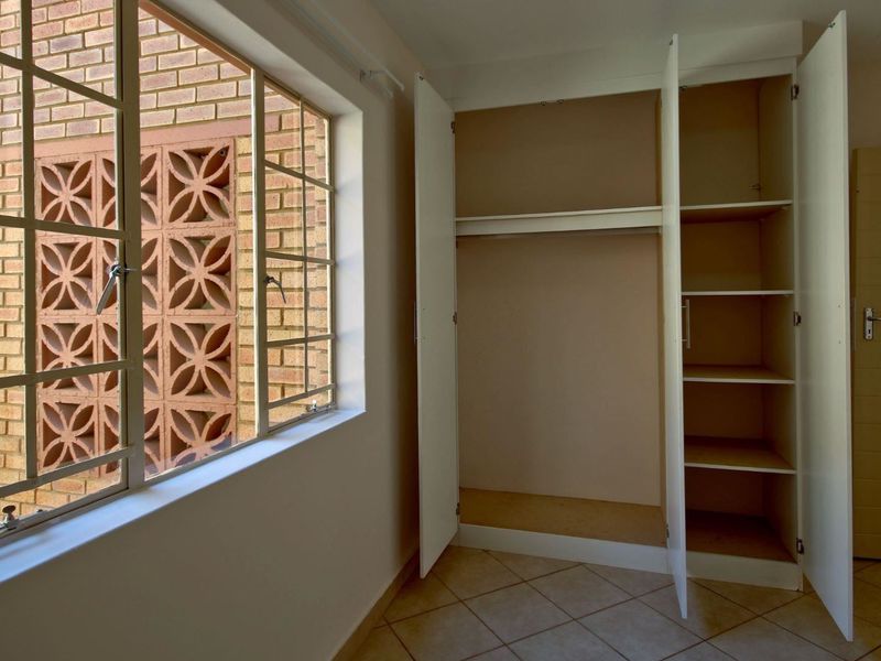 A bright, empty bedroom featuring tiled flooring, a built-in wardrobe with shelving, and a steel-framed window overlooking an exterior brick feature wall.