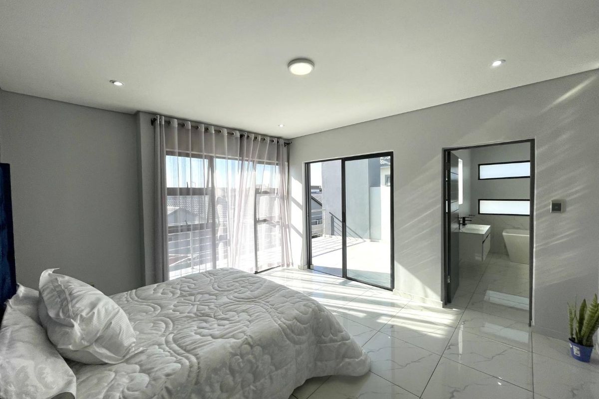 Modern bedroom featuring large format tiled flooring, recessed lighting, and sliding glass doors leading to an outdoor balcony with en-suite bathroom access.