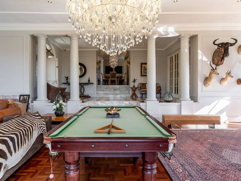Elegant living area featuring rich parquet flooring, classical columns, marble steps, and a grand crystal chandelier, creating a sophisticated and spacious atmosphere.