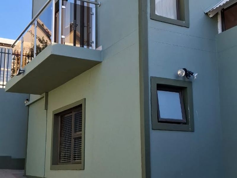 A view of the rear exterior facade featuring a balcony with a glass balustrade, paved driveway, and well-maintained painted walls.