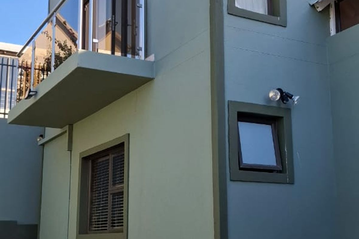 A view of the rear exterior facade featuring a balcony with a glass balustrade, paved driveway, and well-maintained painted walls.
