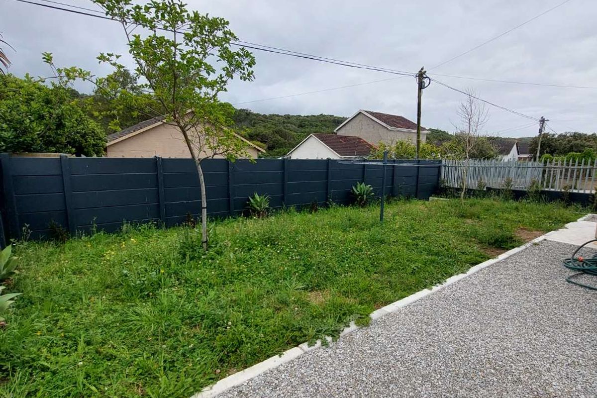 A rear garden featuring a gravel pathway, concrete edging, and a dark-painted precast concrete boundary wall.
