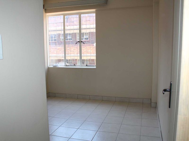 An empty bedroom featuring tiled flooring and a window with security bars, offering a neutral space ready for personalization.