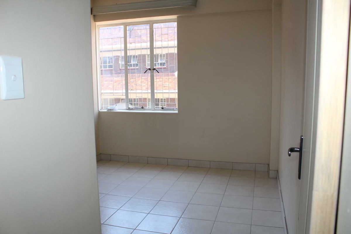 An empty bedroom featuring tiled flooring and a window with security bars, offering a neutral space ready for personalization.