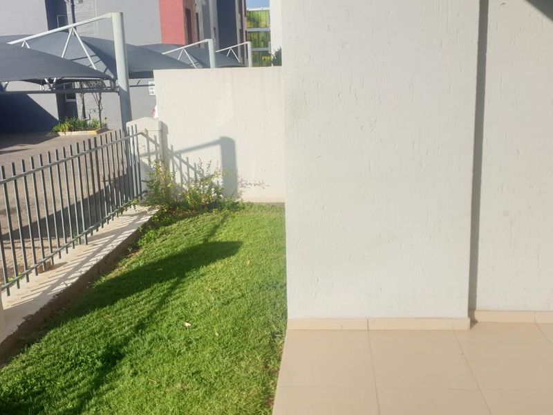 A private ground floor patio area featuring tiled flooring and a small adjacent lawn, enclosed by metal perimeter fencing.