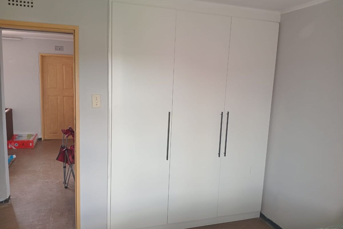 A bedroom featuring built-in white cabinetry with modern handles, providing ample storage space and a clean, neutral aesthetic.