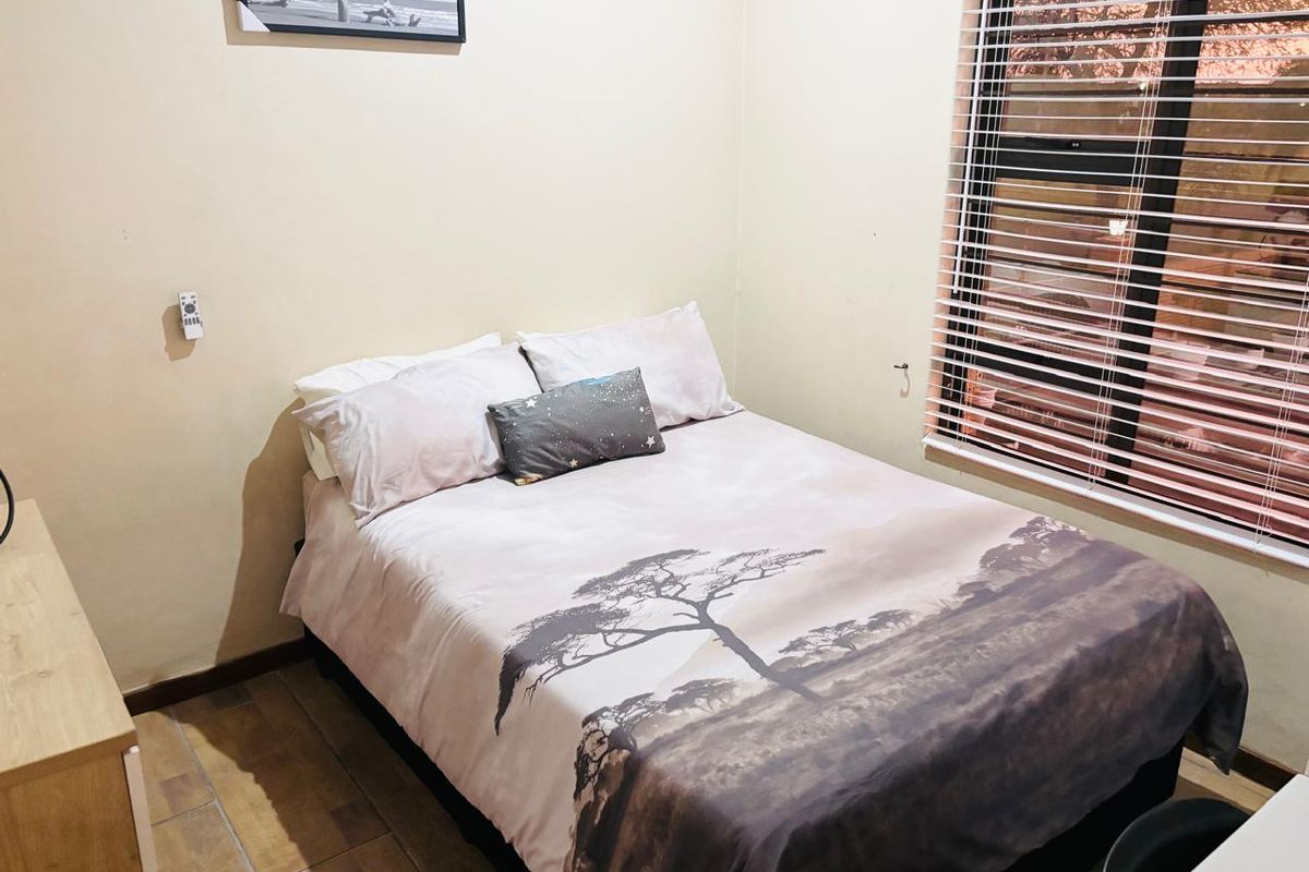 A functional bedroom featuring tiled flooring and a large window fitted with horizontal blinds, providing natural light.