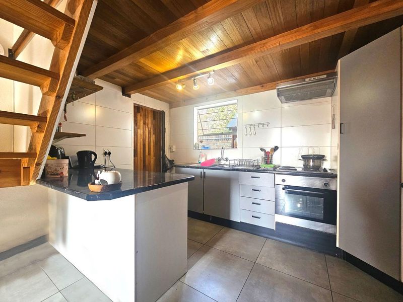 A functional kitchen featuring tiled flooring, timber ceiling beams, a built-in oven with extractor fan, and a breakfast counter adjacent to a timber staircase.