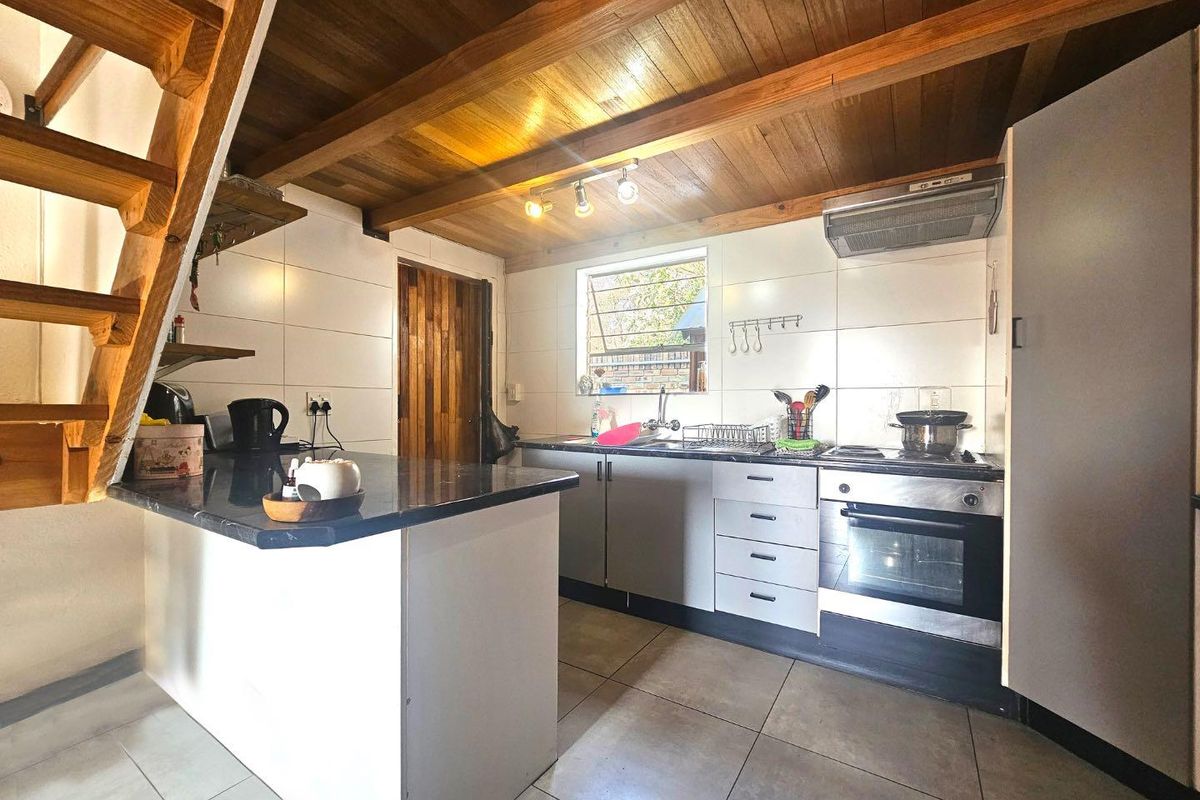 A functional kitchen featuring tiled flooring, timber ceiling beams, a built-in oven with extractor fan, and a breakfast counter adjacent to a timber staircase.