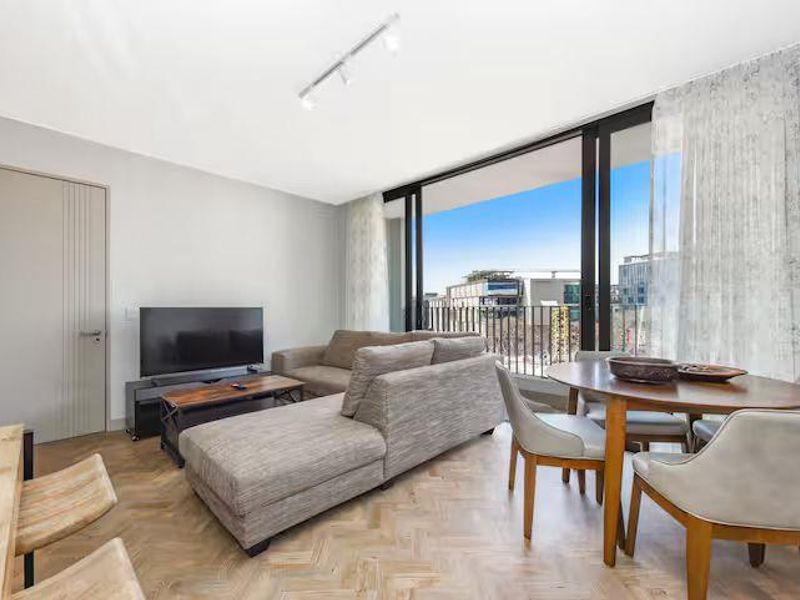Open-plan living and dining area featuring herringbone timber flooring, modern track lighting, and large sliding glass doors opening to a balcony with urban views.