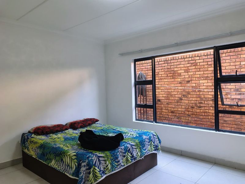 A bedroom featuring tiled flooring and a large window with an aluminium frame, overlooking an exterior brick wall.