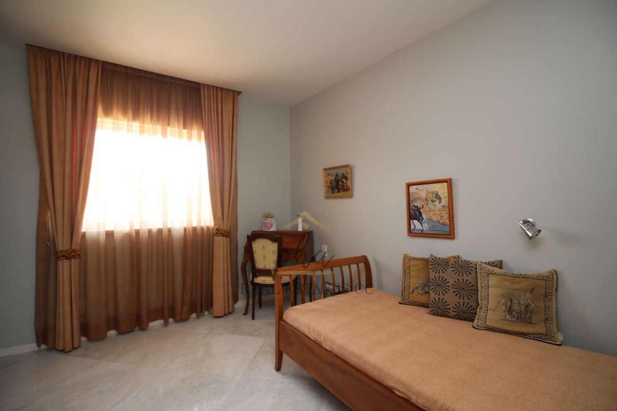 A bedroom featuring marble flooring, neutral wall tones, and a window with floor-to-ceiling curtains.
