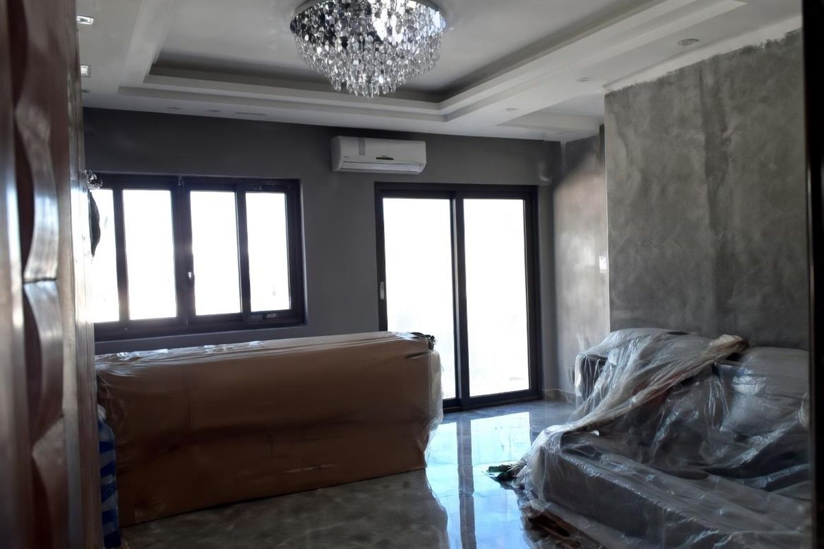 Living room featuring a tray ceiling with crystal chandelier, polished tile flooring, split-system air conditioning unit, and large sliding glass doors.