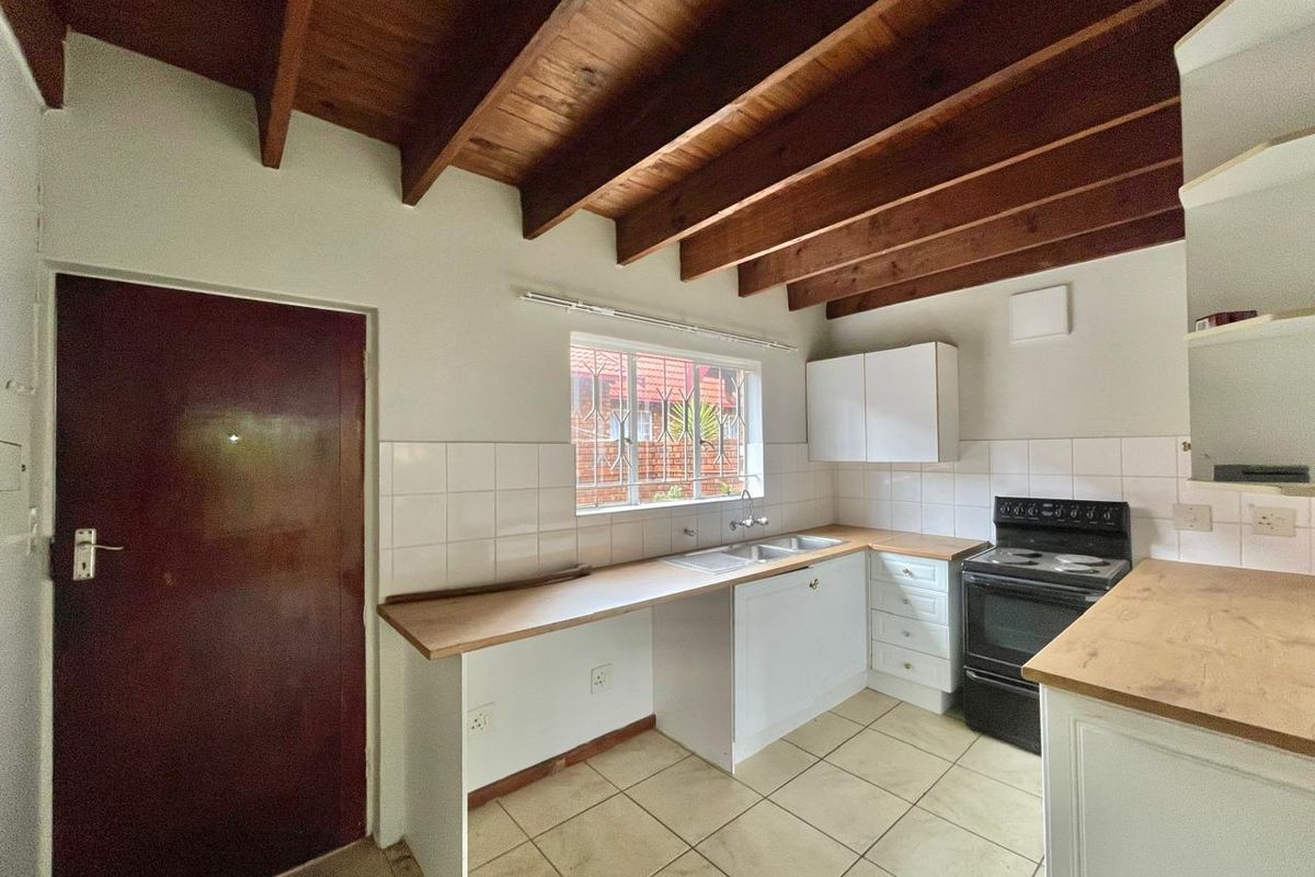 A functional kitchen featuring wooden ceiling beams, tiled flooring, white cabinetry, a double sink, and a freestanding stove.