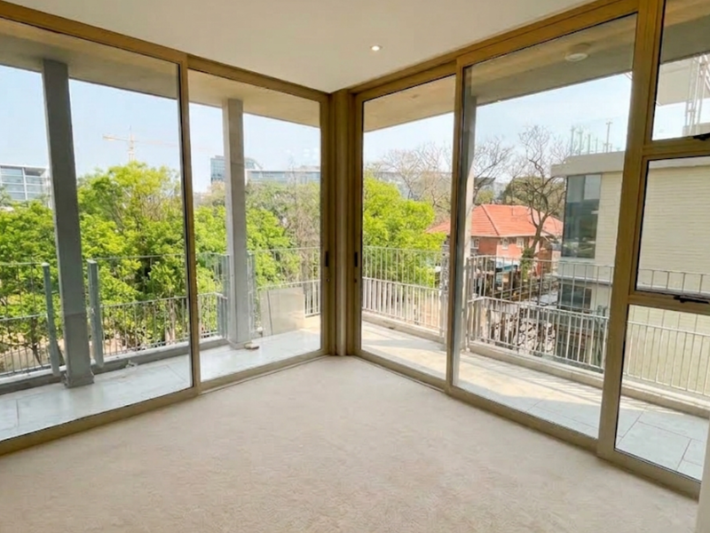A bright, empty living area featuring expansive floor-to-ceiling sliding glass doors that provide abundant natural light and access to a wrap-around balcony.
