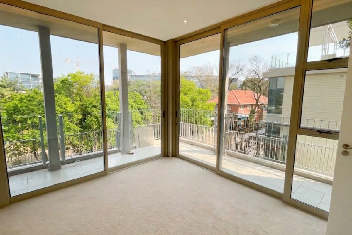 A bright, empty living area featuring expansive floor-to-ceiling sliding glass doors that provide abundant natural light and access to a wrap-around balcony.