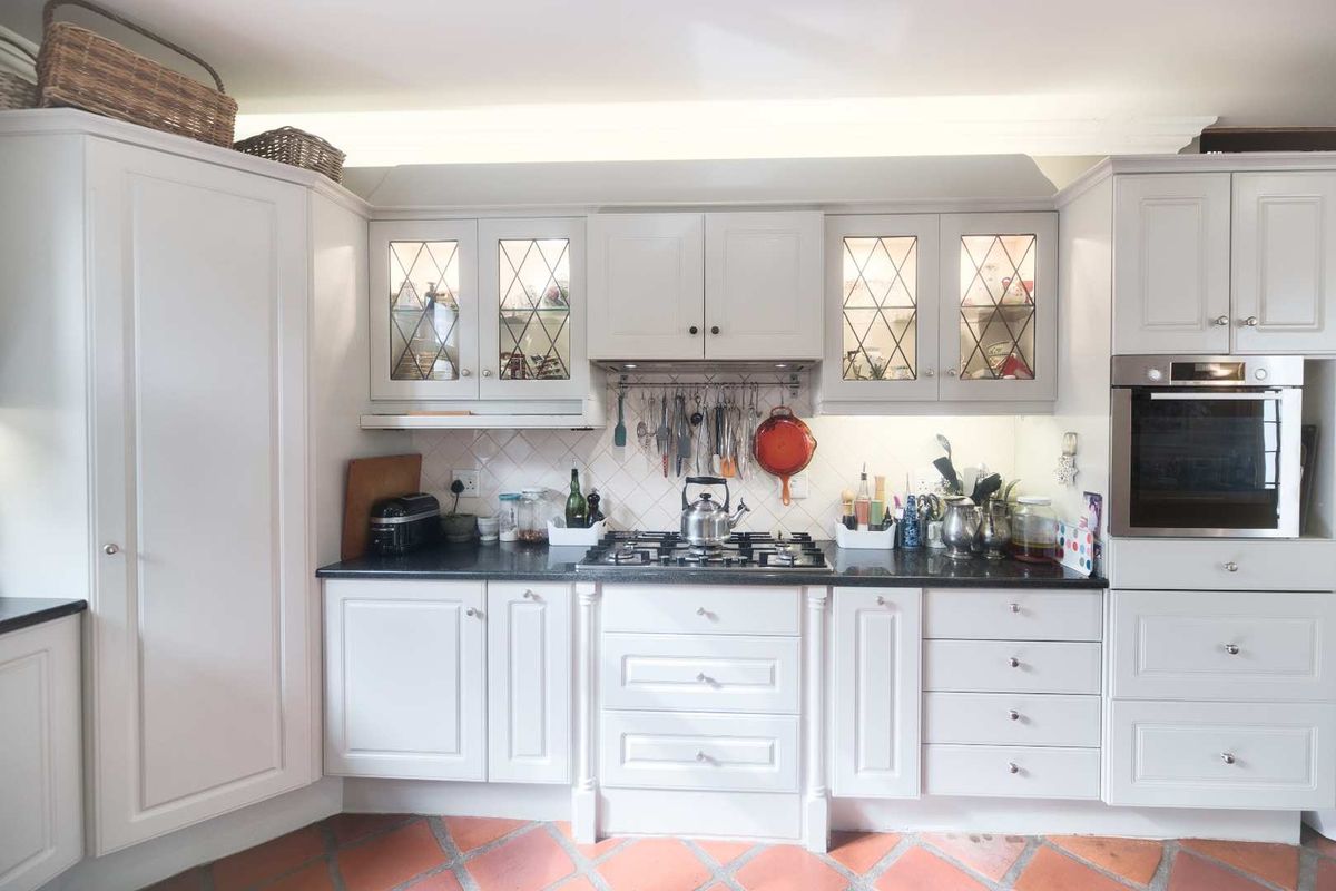 A well-maintained kitchen featuring white cabinetry, a gas hob, built-in oven, extractor fan, and classic terracotta floor tiles.