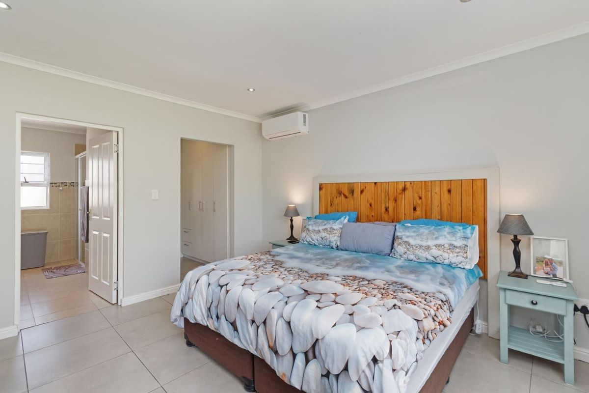Spacious bedroom featuring tiled flooring, built-in cupboards, and a wall-mounted air conditioning unit, with an adjoining en-suite bathroom.