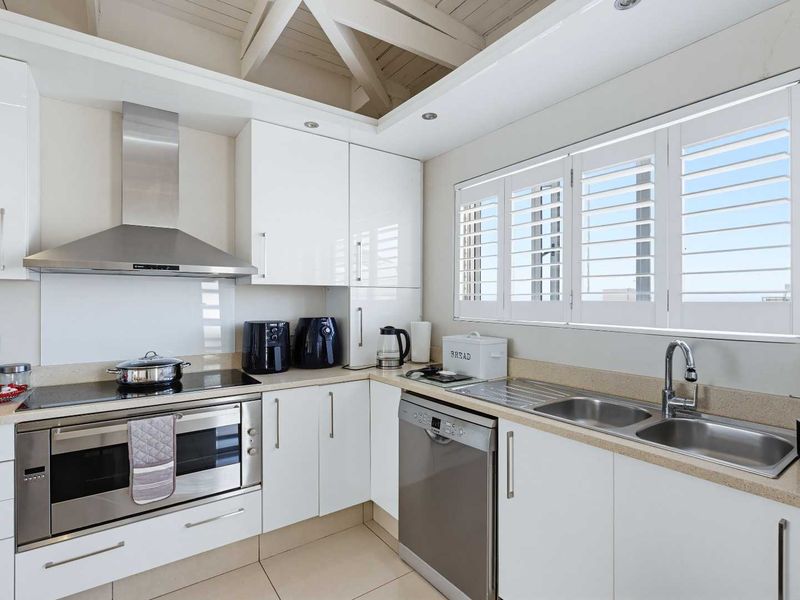 Modern kitchen featuring white high-gloss cabinetry, stone countertops, stainless steel appliances, and plantation shutters under an exposed beam ceiling.