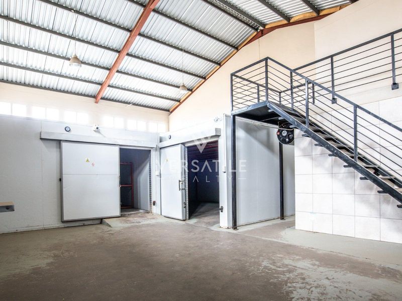 Industrial utility space featuring cold storage units, exposed steel roof structure, and a metal staircase leading to an upper level.