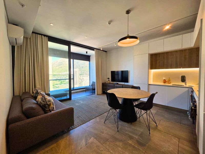 Modern open-plan living area featuring a sleek kitchen with built-in cabinetry, tiled floors, and large sliding doors opening to a balcony with scenic views.