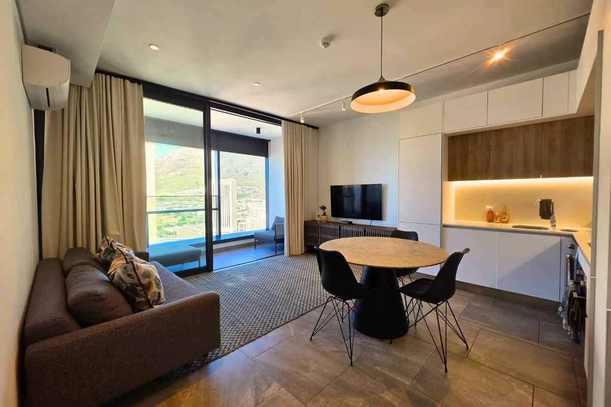 Modern open-plan living area featuring a sleek kitchen with built-in cabinetry, tiled floors, and large sliding doors opening to a balcony with scenic views.