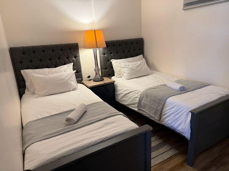 A compact bedroom featuring two single beds with tufted headboards and wood-look flooring.