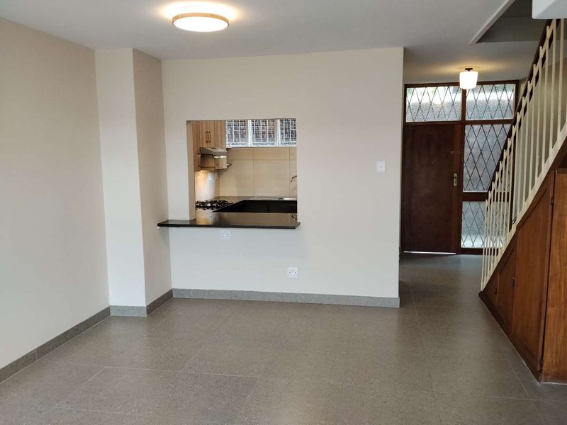 Open plan living area featuring tiled floors, a kitchen pass-through window with granite counter, and a classic timber staircase leading to the upper level.