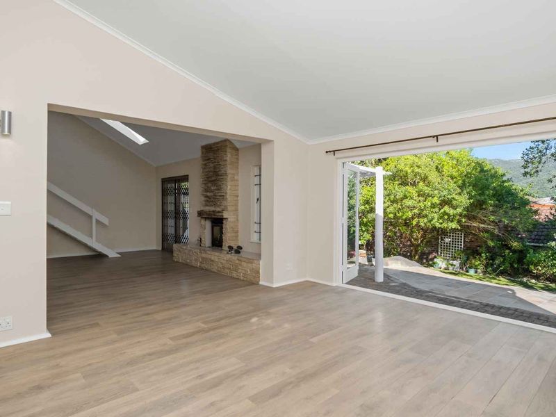 Spacious living area featuring light laminate flooring, a stone-clad fireplace, and large bi-fold doors opening to a private garden.