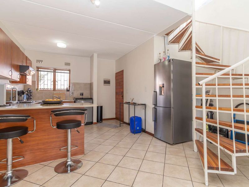 Open-plan kitchen area featuring wood-finish cabinetry, tiled flooring, and a prominent spiral staircase leading to the upper level.