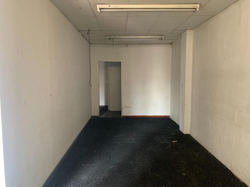 An empty, dated office space featuring worn carpeting, suspended ceiling tiles, and fluorescent lighting, ready for renovation or refurbishment.