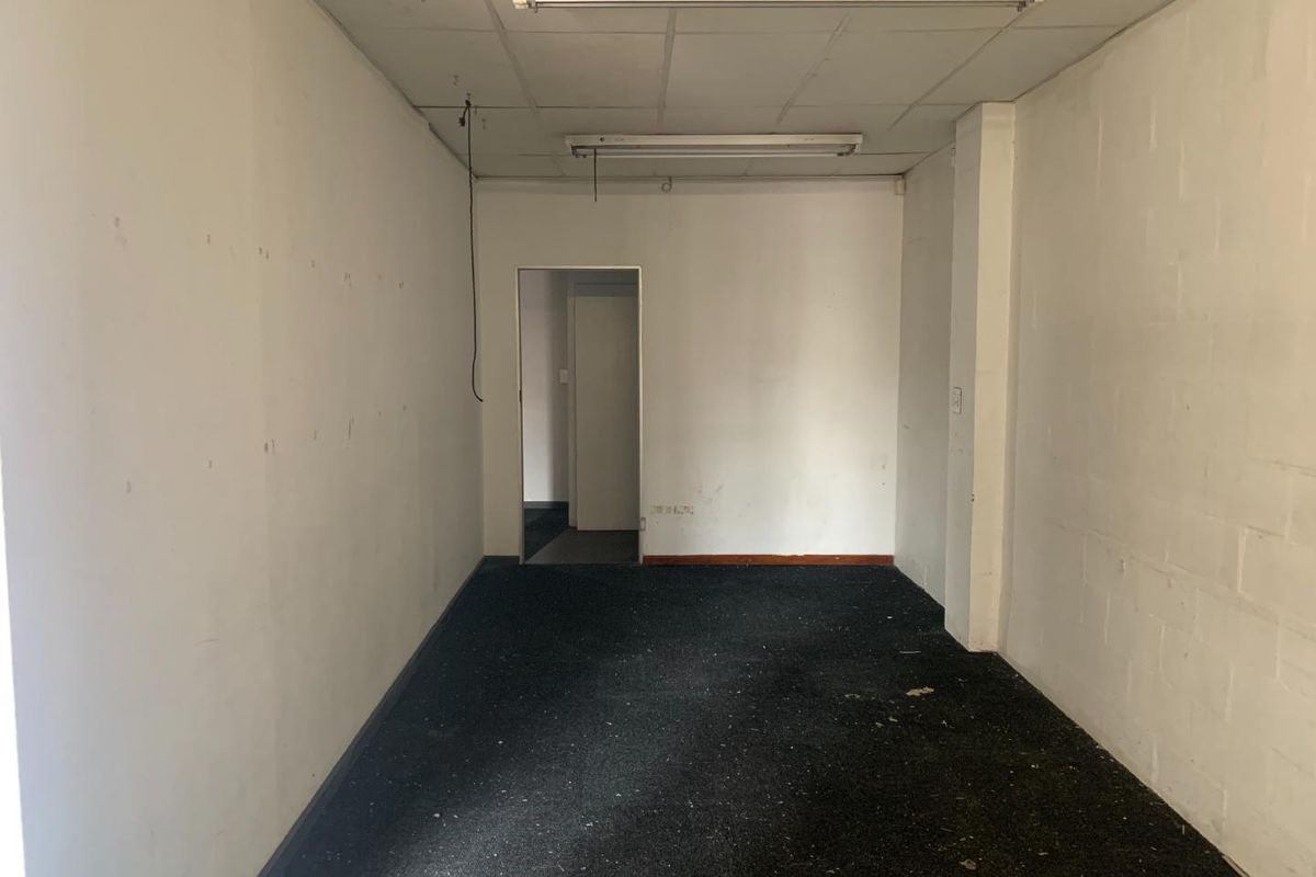 An empty, dated office space featuring worn carpeting, suspended ceiling tiles, and fluorescent lighting, ready for renovation or refurbishment.