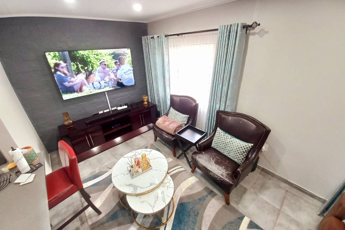 A cozy living room featuring a dark textured accent wall, tiled flooring, and a large wall-mounted television.