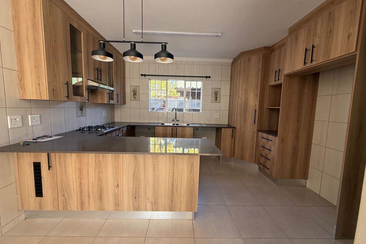 Modern kitchen featuring wood-grain cabinetry, dark stone countertops, a built-in gas hob, extractor fan, and tiled flooring.