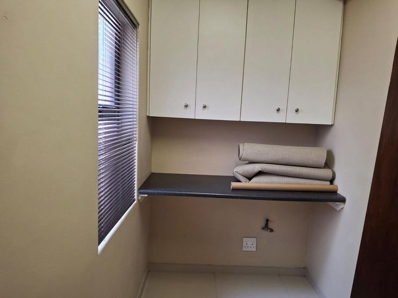 A functional laundry area featuring built-in overhead cabinetry, a laminate work surface, and plumbing connections for a washing machine.