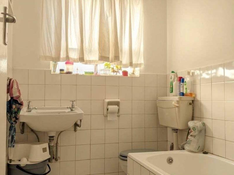 A functional bathroom featuring a wall-mounted basin, built-in bathtub, and tiled finishes, offering potential for modernization and cosmetic updates.