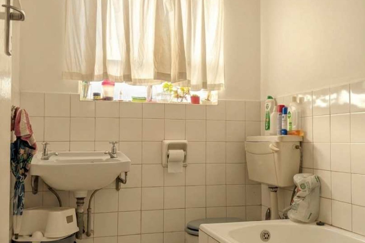A functional bathroom featuring a wall-mounted basin, built-in bathtub, and tiled finishes, offering potential for modernization and cosmetic updates.