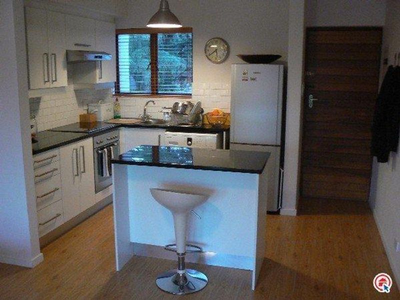 A compact, modern kitchen featuring white cabinetry, granite countertops, subway tile backsplash, and a functional breakfast island with pendant lighting.