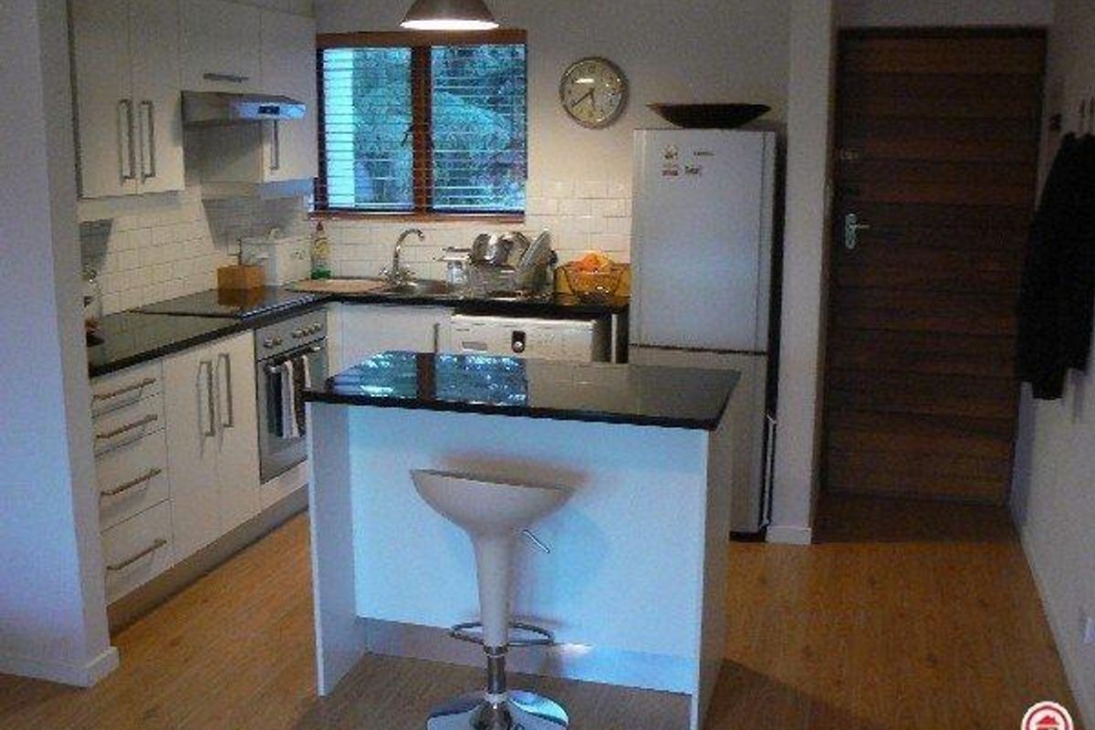 A compact, modern kitchen featuring white cabinetry, granite countertops, subway tile backsplash, and a functional breakfast island with pendant lighting.