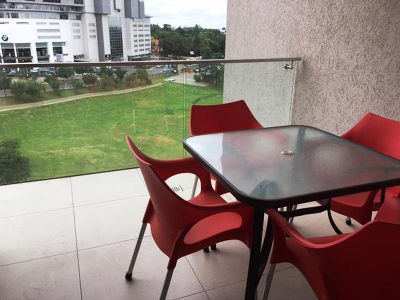 A modern balcony featuring a sleek glass balustrade, large format floor tiles, and a textured wall finish, offering an open view of the surrounding area.