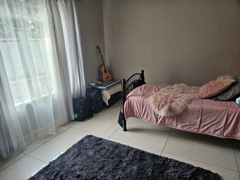 A bedroom featuring tiled flooring and a window with security bars, providing a functional and well-lit living space.